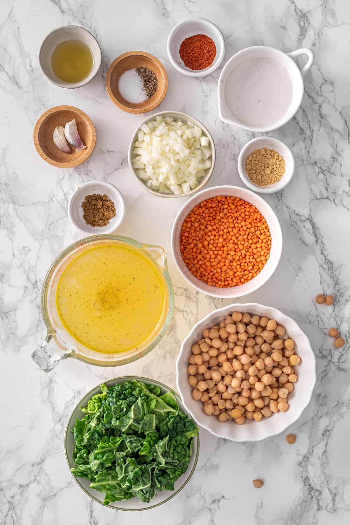 Chickpea Lentil Soup ingredients on marble: red lentils, chickpeas, chopped kale, vegetable broth, diced onion, coconut cream, smoked paprika, cumin,
