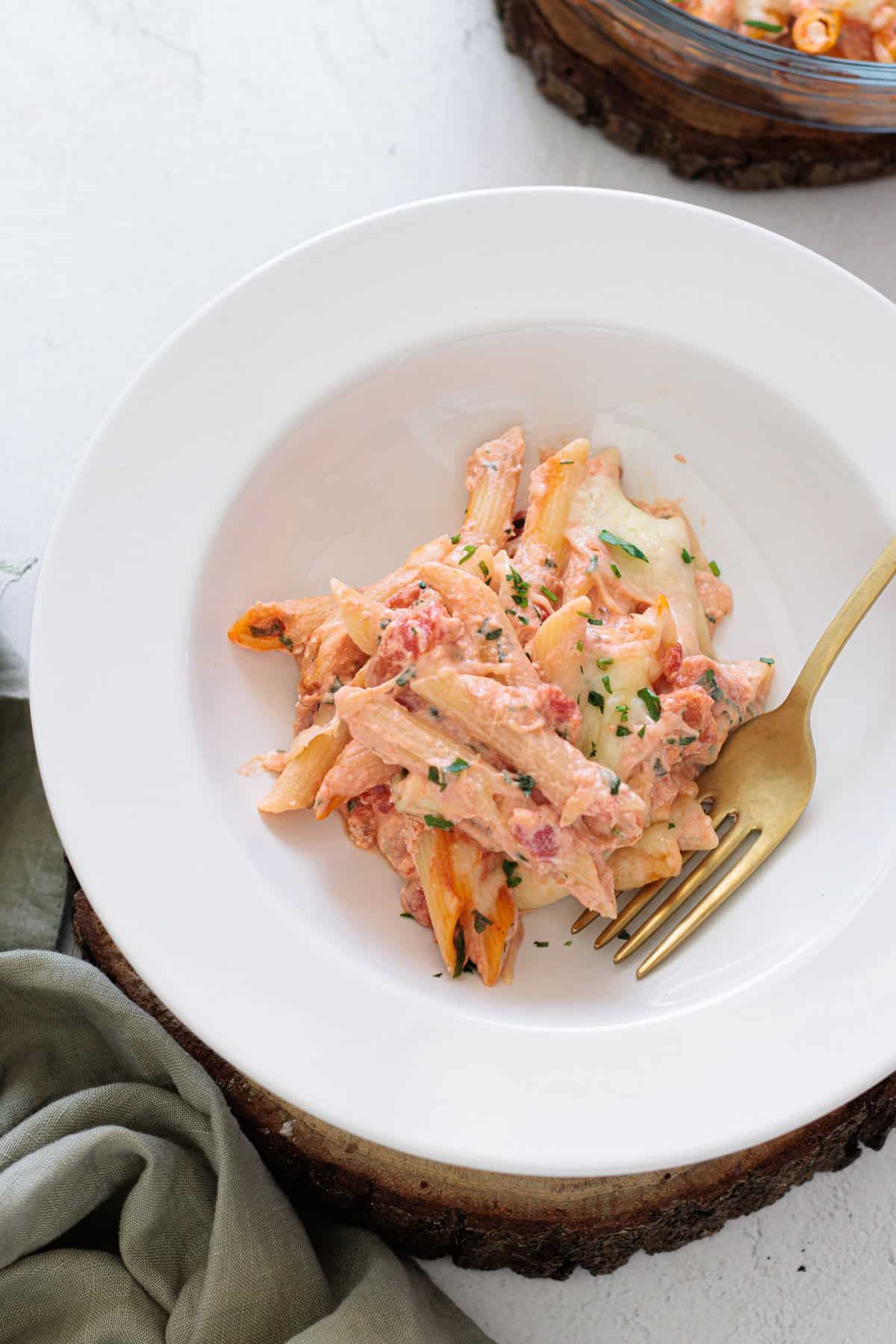 Easy Cheesy Red Lentil Baked Ziti served in a white bowl on a wood slice with a gold fork and sage green linen napkin