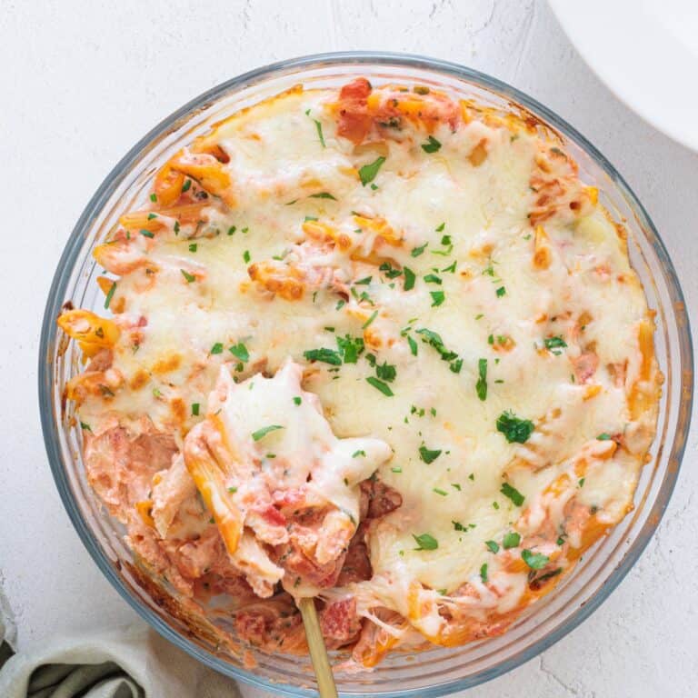 Easy Cheesy Red Lentil Baked Ziti in a round glass baking dish, topped with melted mozzarella and fresh parsley, spoon lifting a cheesy serving