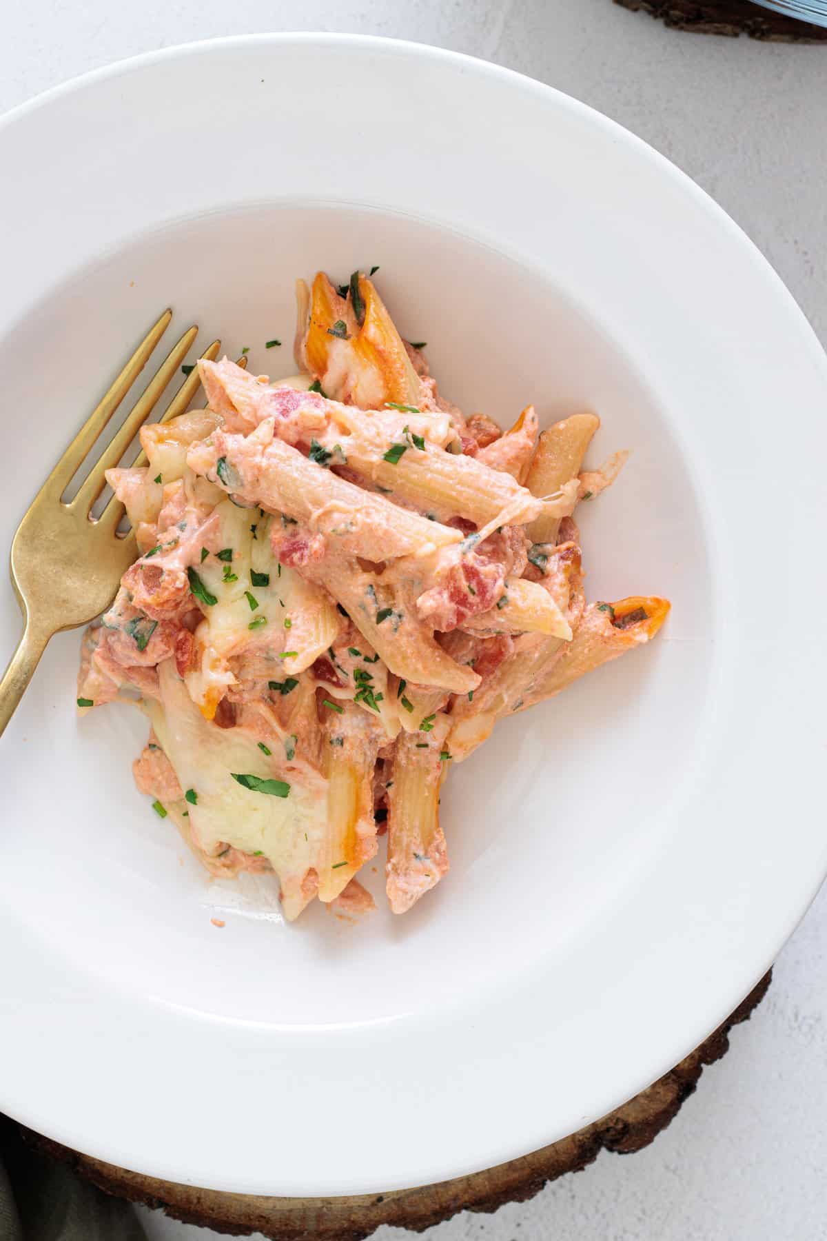 Easy Cheesy Red Lentil Baked Ziti served on a white plate with a gold fork, topped with melted cheese and fresh herbs