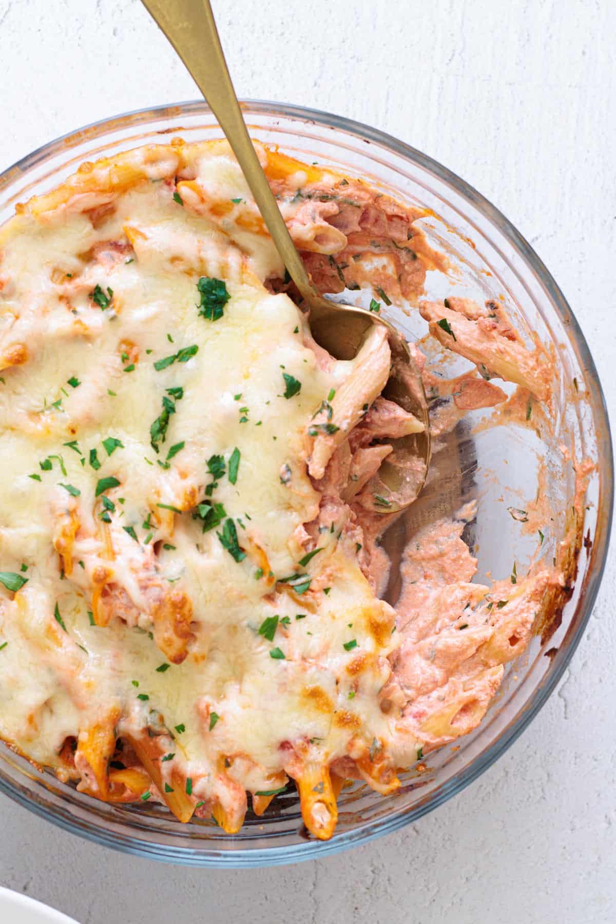 Easy Cheesy Red Lentil Baked Ziti in a glass baking dish with melted mozzarella and fresh parsley, served with a gold spoon