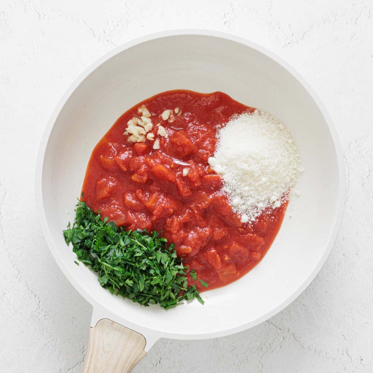 White skillet with crushed tomatoes, minced garlic, grated parmesan, and chopped parsley for Easy Cheesy Red Lentil Baked Ziti