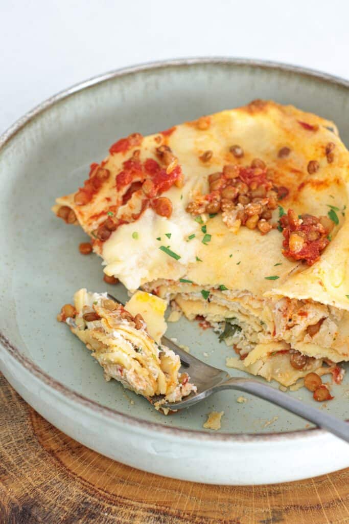 Plated slice of vegan lentil lasagna with lentil tomato sauce, creamy layers, and fresh herbs on a sage ceramic plate with a fork.