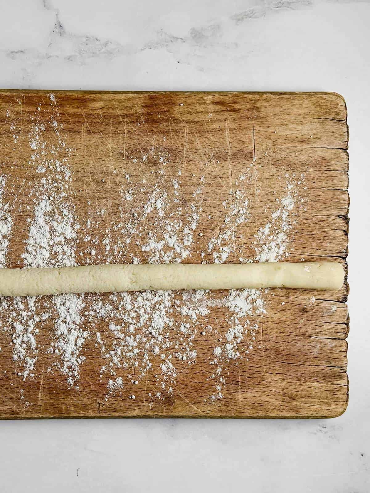 log of soft dough rolled into a thin rope on a flour-dusted wooden board