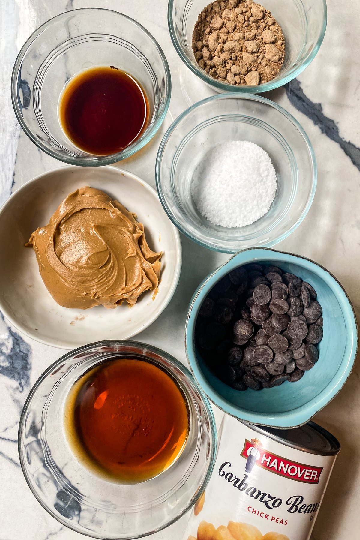 Chickpea Cookie Dough ingredients in bowls: creamy peanut butter, maple syrup, coconut sugar, salt, vanilla extract, and dairy-free chocolate chips
