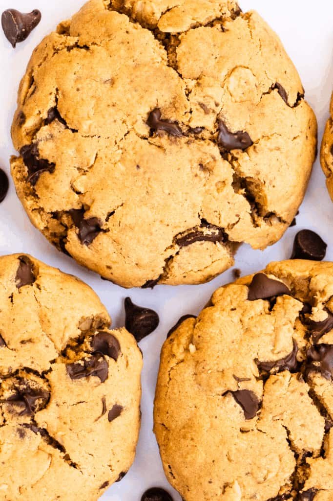 close-up of thick chocolate chip cookies with melty chocolate chunks scattered on a white surface
