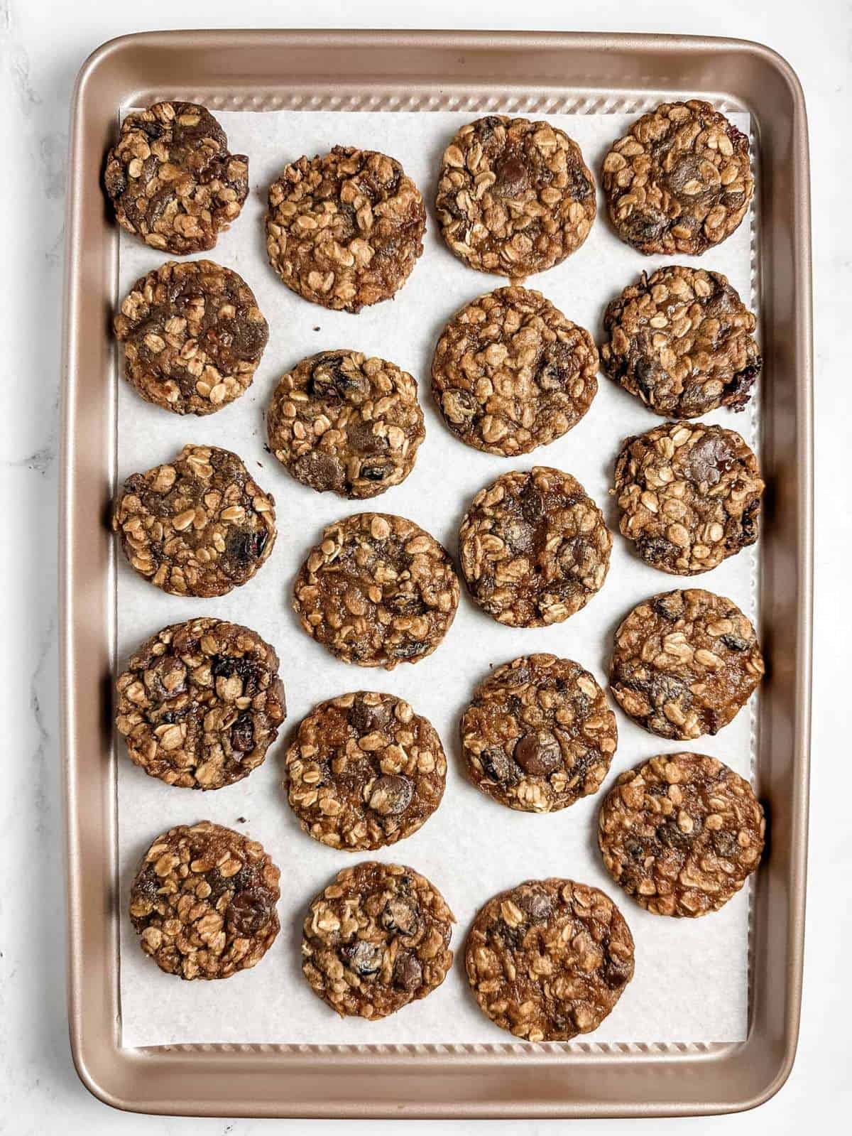 overhead view of vegan oatmeal cookies arranged on a parchment-lined gold baking sheet