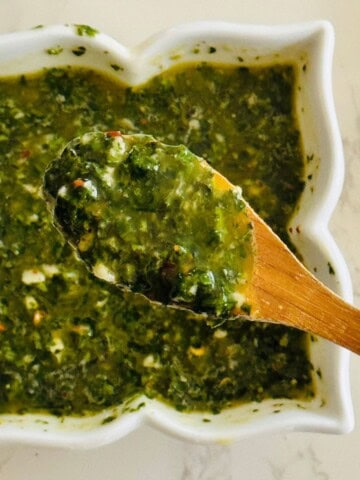 close up of a wooden spoon full of basil chimichurri sauce