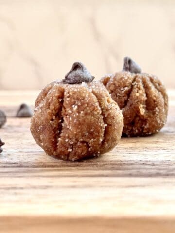 set of 2 pumpkin protein balls on a wooden board with chocolate chips on the side.