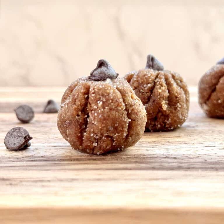 set of 2 pumpkin protein balls on a wooden board with chocolate chips on the side.