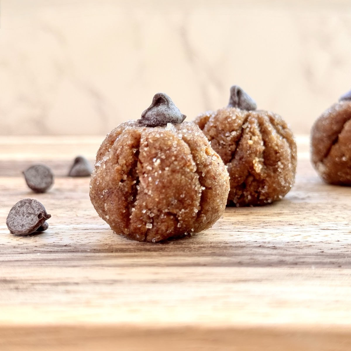 set of 2 pumpkin protein balls on a wooden board with chocolate chips on the side.