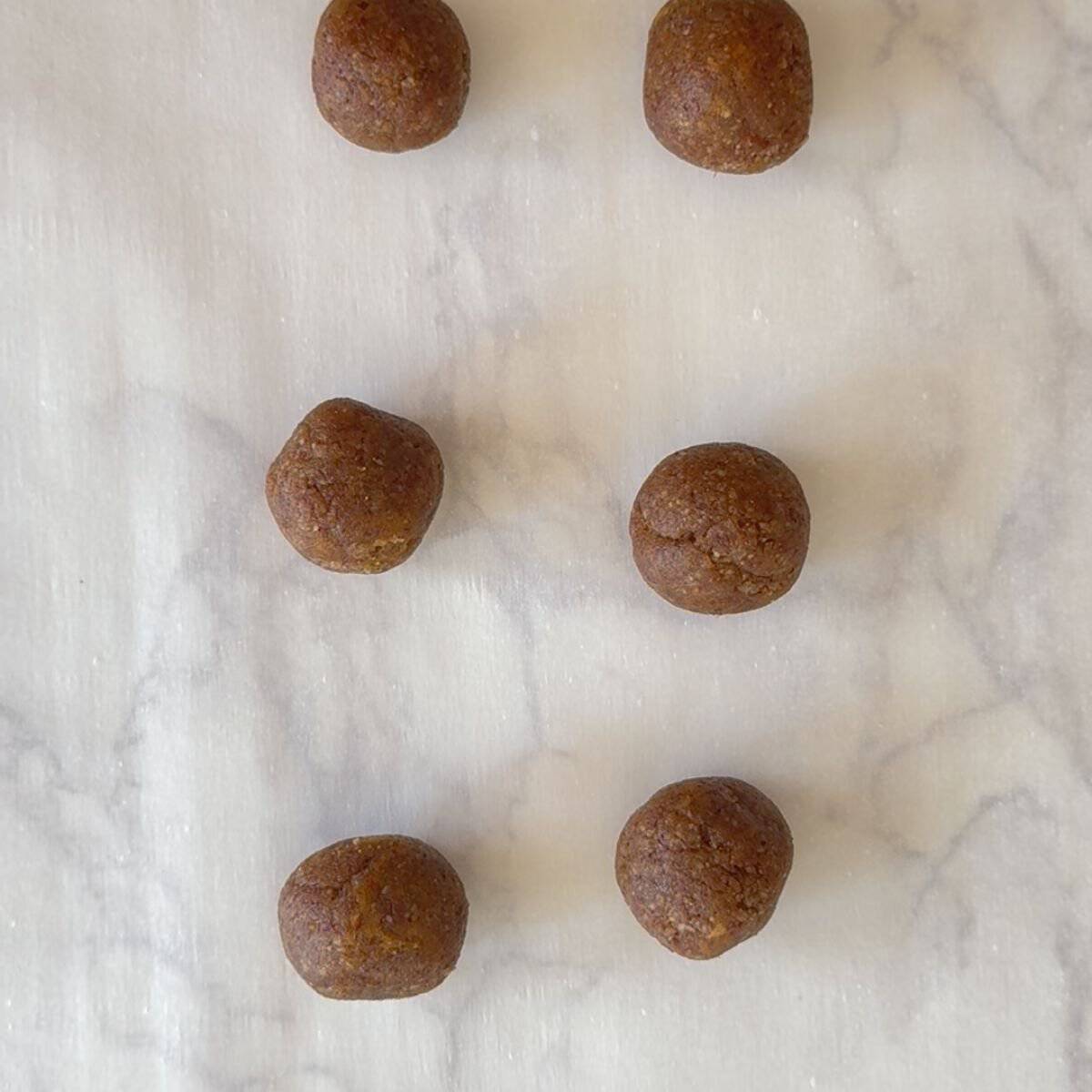 Six unbaked pumpkin spice protein balls rolled in coconut sugar arranged on a marble surface