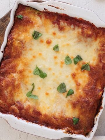 Baked spinach ricotta lasagna in a white square baking dish with golden browned mozzarella and fresh basil leaves on top.