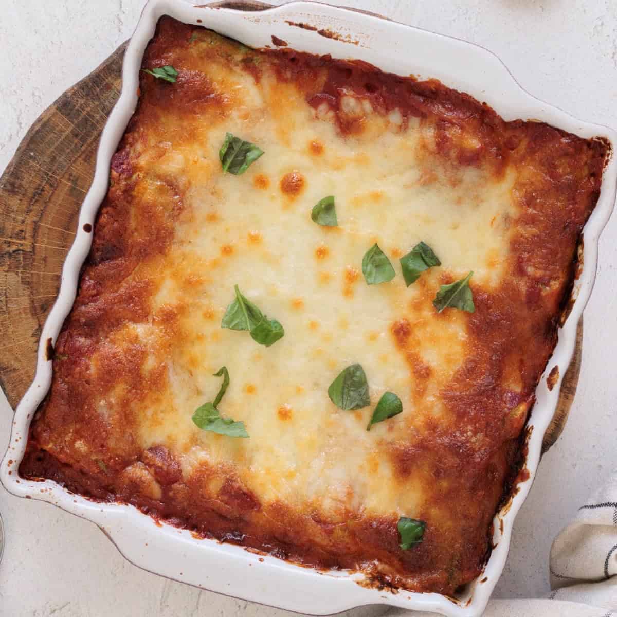 Baked spinach ricotta lasagna in a white square baking dish with golden browned mozzarella and fresh basil leaves on top.
