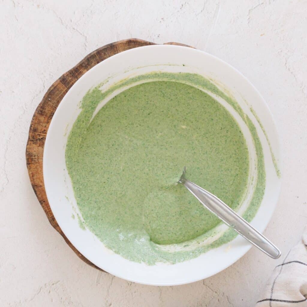 Smooth green blended spinach ricotta filling in a white bowl with a spoon.
