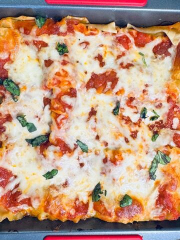 Spinach Ricotta Lasagna baked in a square pan topped with melted shredded mozzarella, marinara sauce, and fresh basil leaves.