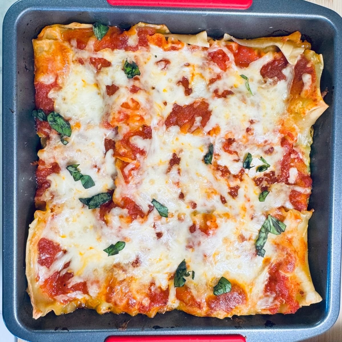 Spinach Ricotta Lasagna baked in a square pan topped with melted shredded mozzarella, marinara sauce, and fresh basil leaves.